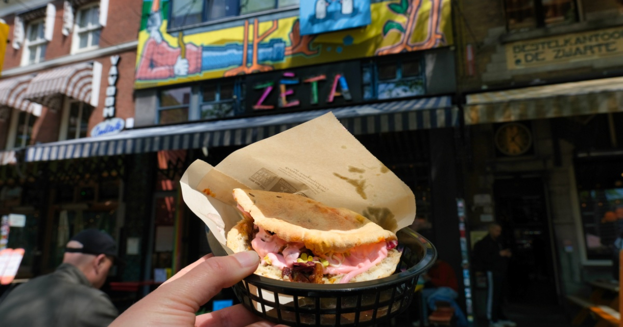 Eine Hand hält ein Sandwich vor einem bunten Restaurant