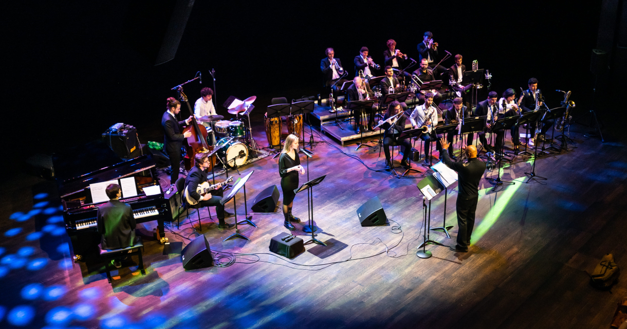 Een bigband speelt muziek op een podium met muzikanten en zangers.