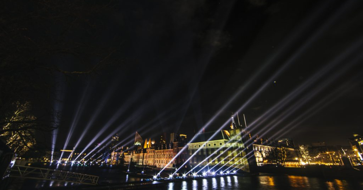 Lasershow boven de Hofvijver voor het aftelmoment met publiek en het Binnenhof op de achtergrond.