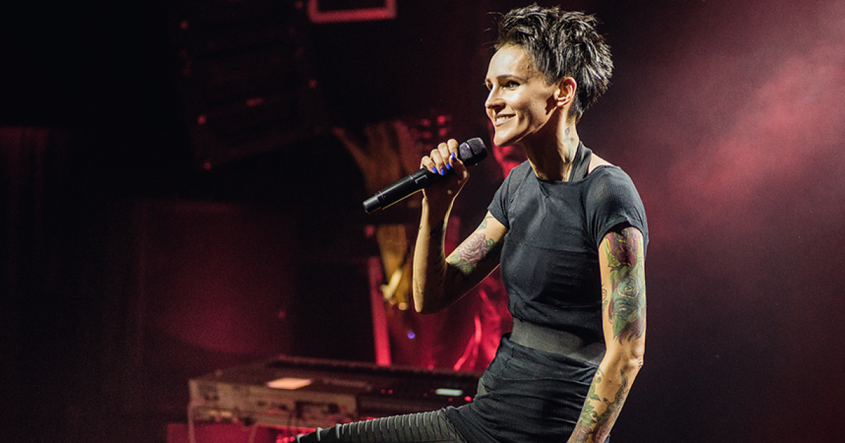Een zangeres met tattoos performt op het podium.