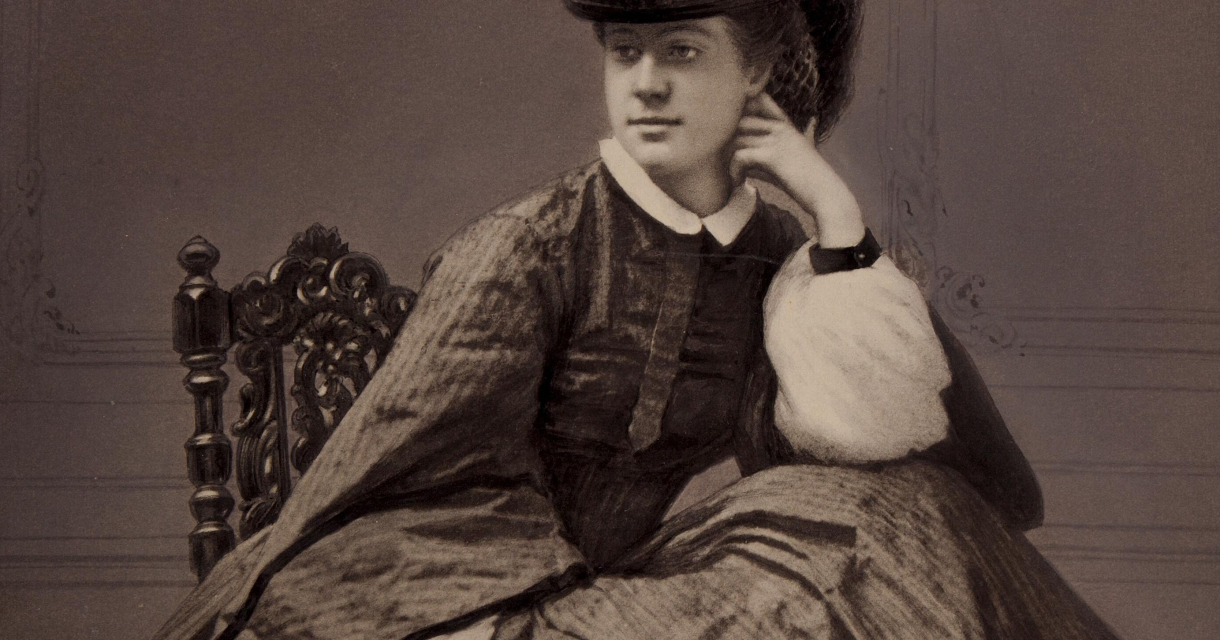 Een vrouw in een elegant, 19e-eeuws kostuum, zittend op een stoel. (c) Robert Jefferson Bingham