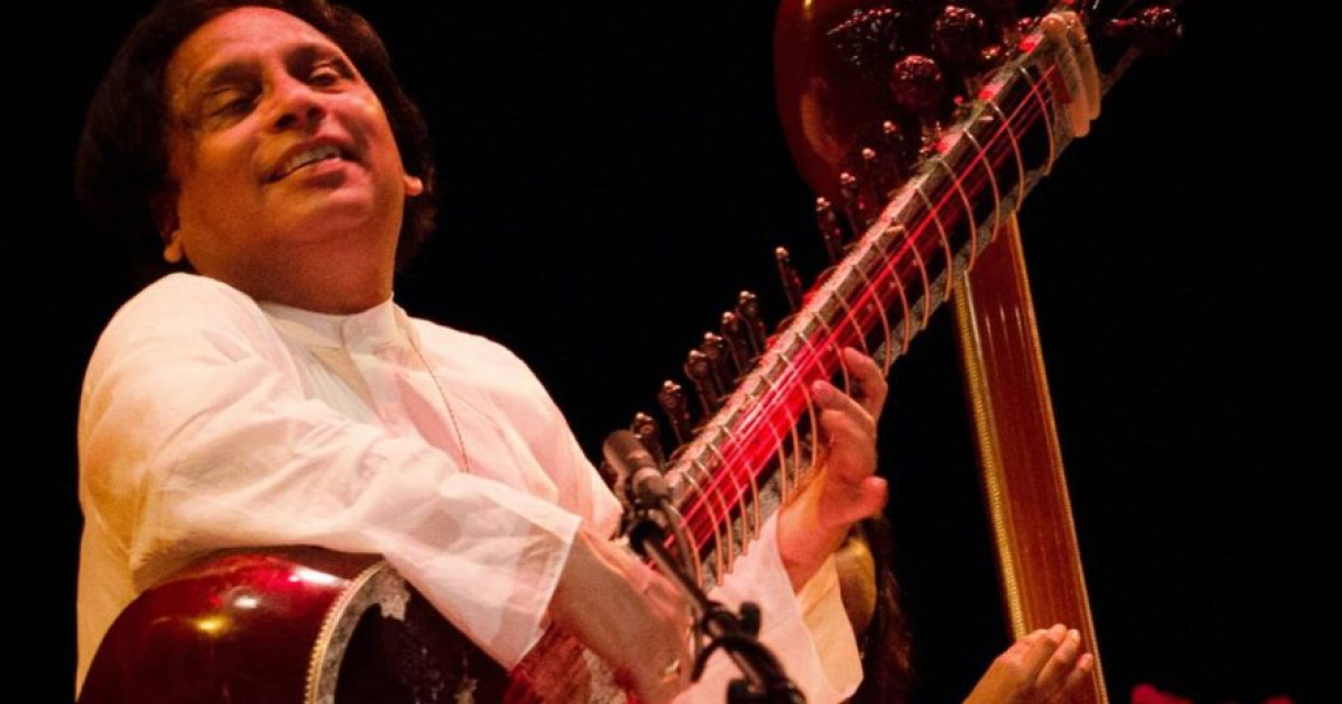 Een muzikant speelt op een sitar met een glimlach.