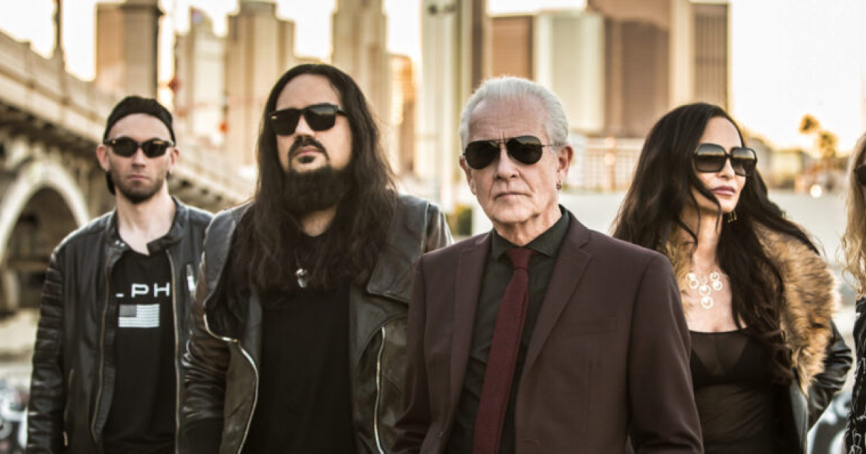 Vijf mensen in leren jassen en zonnebrillen staan samen in het stadsleven.