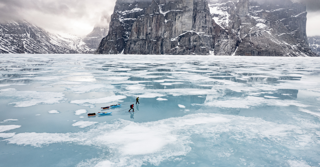 Two skiers on a frozen lake surrounded by mountains.