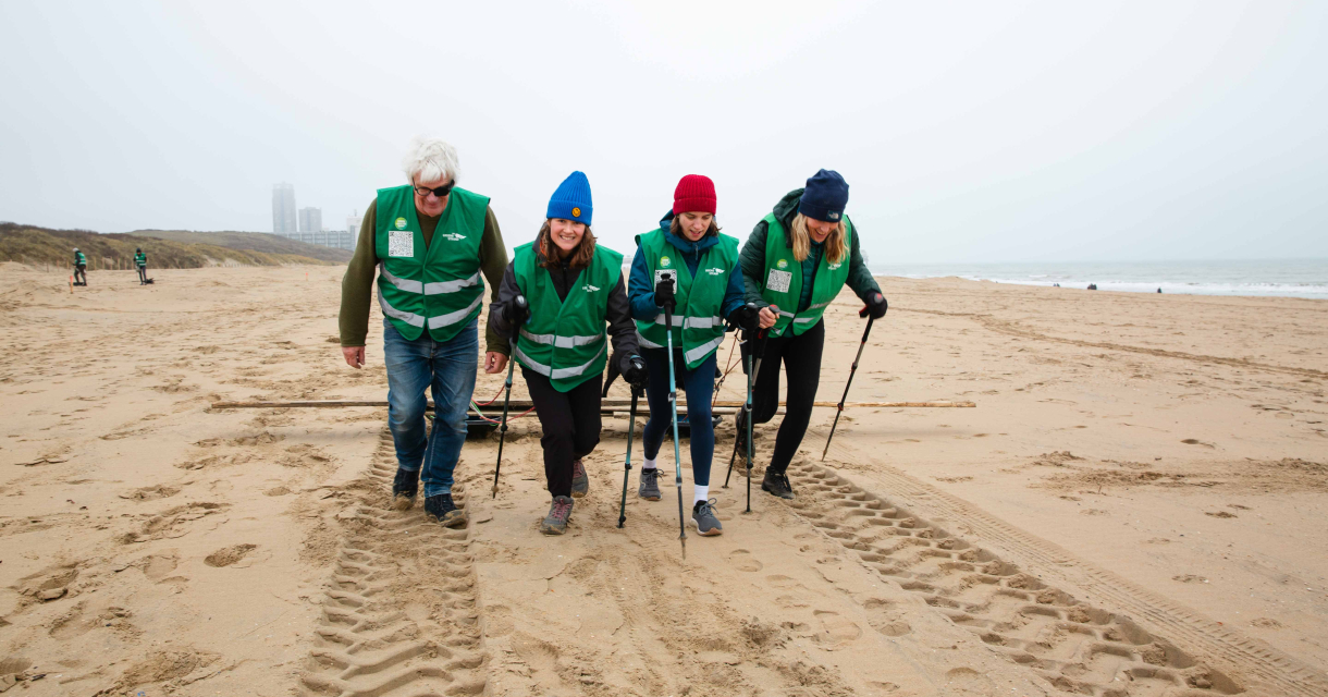 Volunteers in green vests walking on the beach. (c) Eveline van Egdom