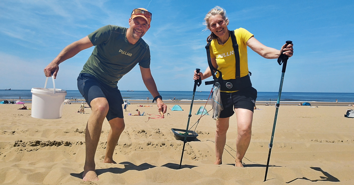 A man and woman stand on the beach, he wears a T-shirt and shorts, she in a yellow shirt and activewear.