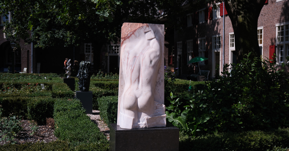 Aanzicht van een marmeren beeld in een groene tuin.