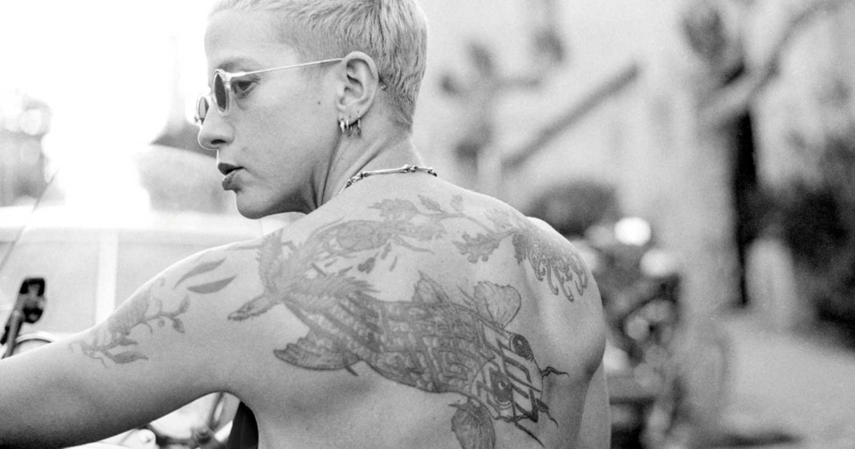 Portret van een persoon met korte haren en een tatoeage op de rug.