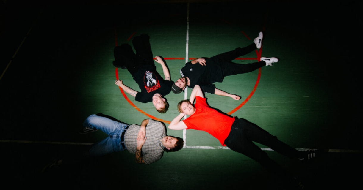 Vijf jongeren liggen op een sportveld in een cirkel.