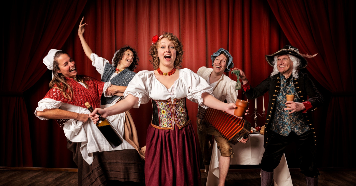 Vijf mensen in historische kostuums vieren met drinken en muziek.