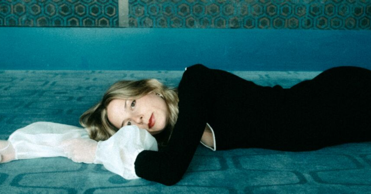 Een vrouw ligt op een blauw tapijt met een zwarte jurk aan.