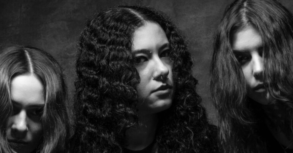Drie vrouwen van band Crypta met krullend haar kijken serieus in de camera.