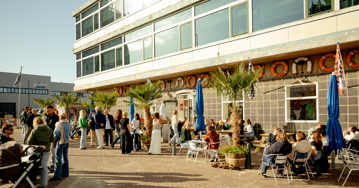 Mensen op een zonnig terras bij het Zeemanshuis in de haven van Scheveningen, omringd door palmbomen en maritieme details  @charlottevdgaag