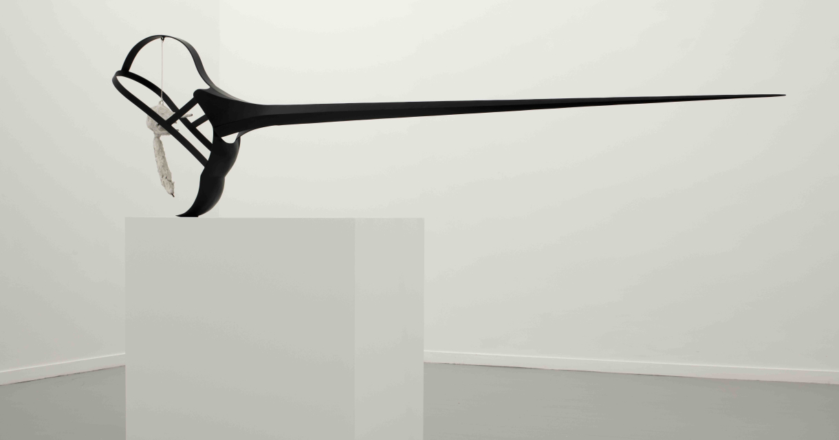 Een lange, zwarte abstracte sculptuur staat op een witte sokkel.