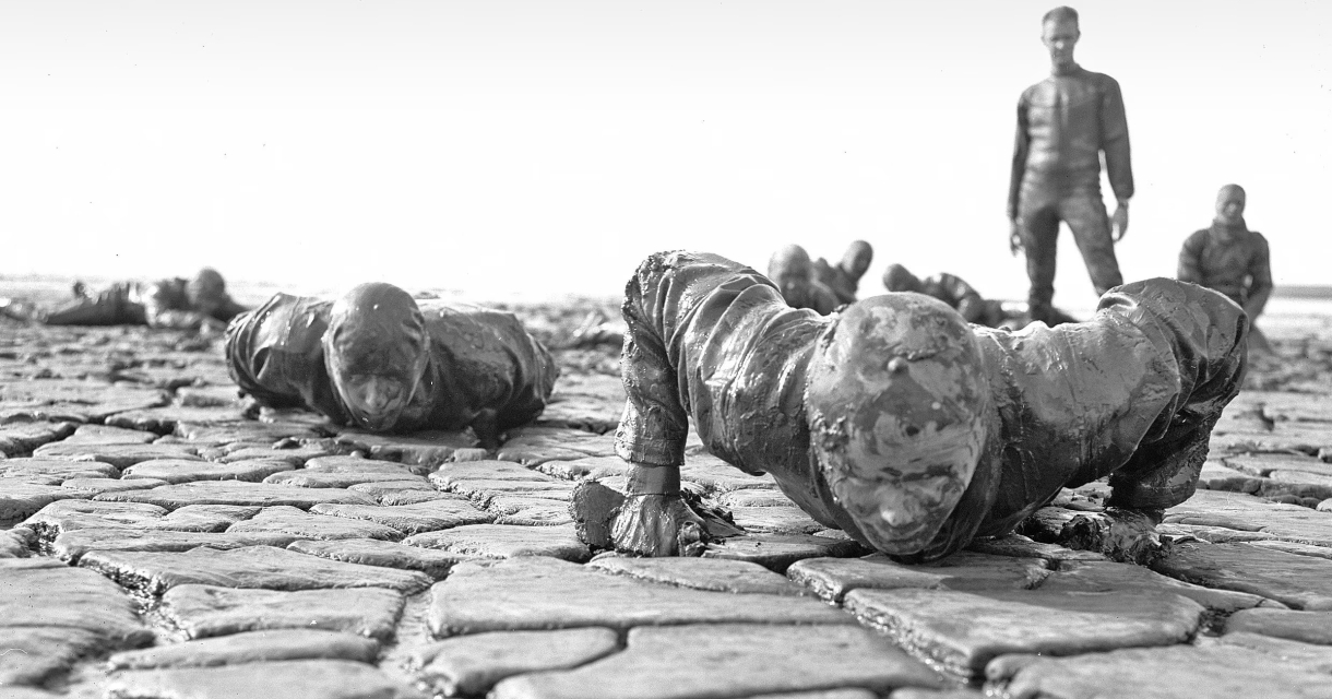 Dag van de Militaire geschiendenis. Mannen in wetsuits doen push-ups op een klei-achtige ondergrond.