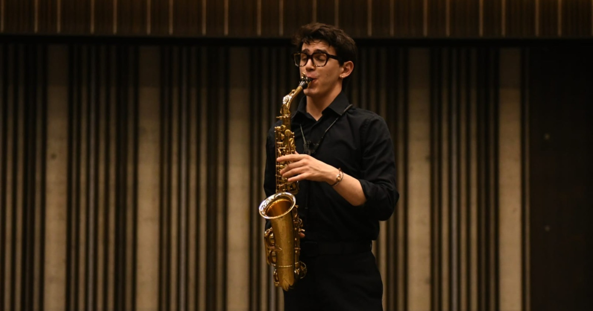 Een jonge saxofonist speelt in een zaal.