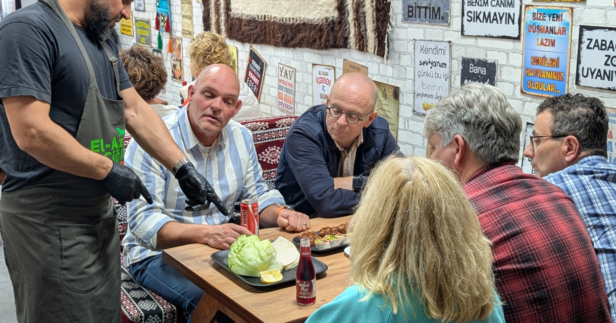 Een man wijst naar een gerecht terwijl anderen attent kijken. Een man wijst naar een gerecht terwijl anderen attent kijken.
