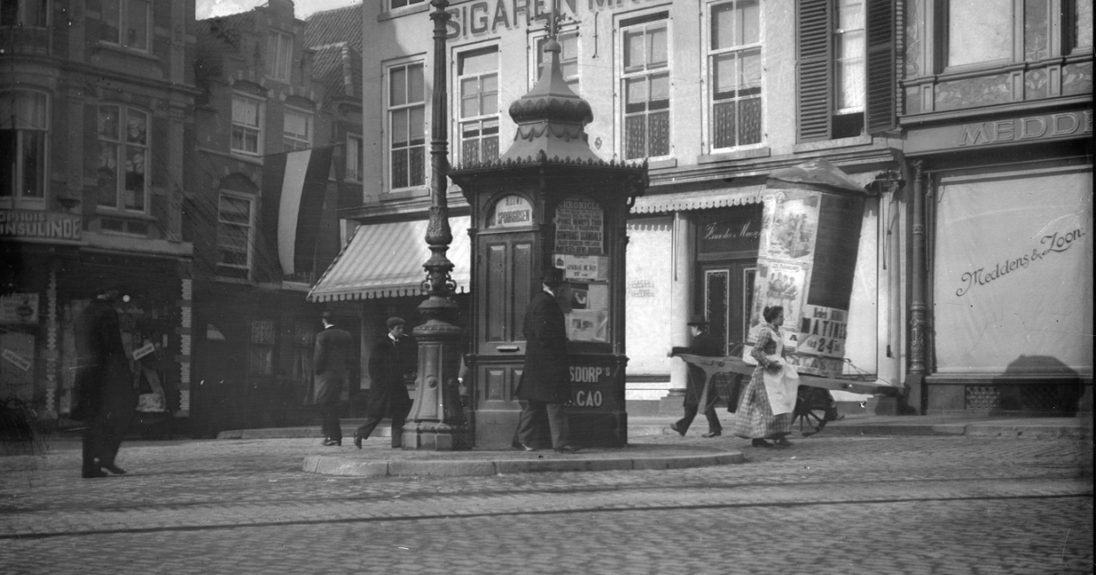 Zicht op een historische straat met een kiosk en mensen.
