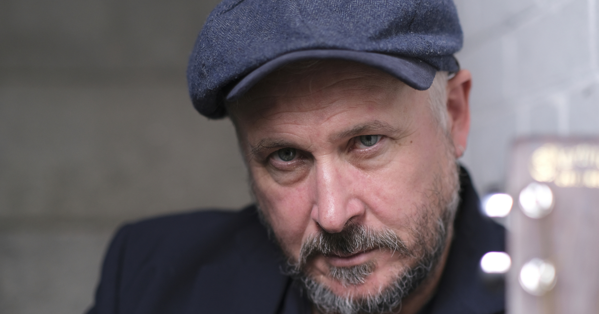 Een man met een hoed kijkt serieus in de camera.