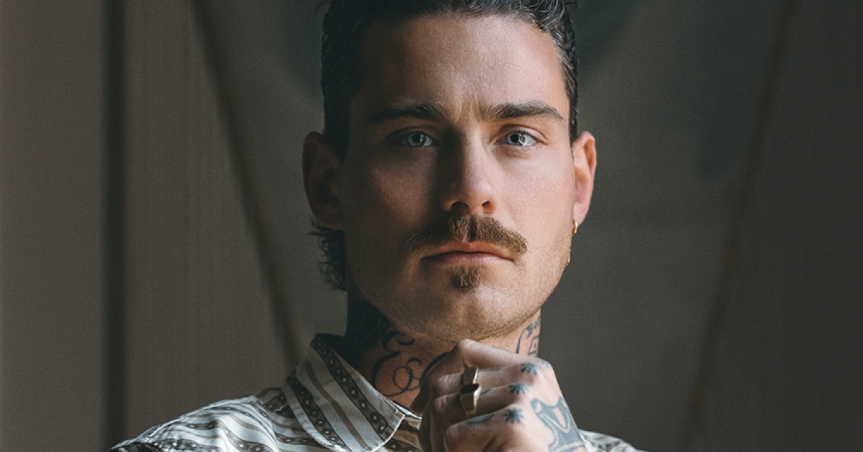 Portret van Douwe Bob met snor en serieus kijkend.