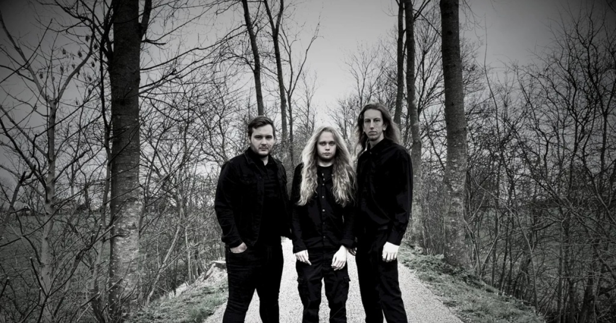 Drie mannen in het zwart staan op een smal pad omringd door bomen.