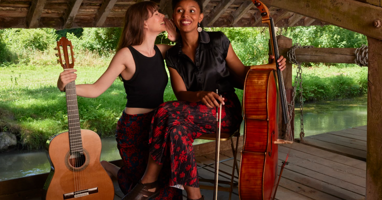 Twee vrouwen lachen met een gitaar en een cello op een houten steiger