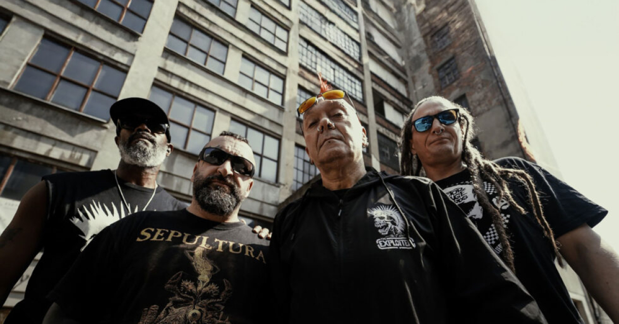 Muzikanten bij een groot gebouw. Vier muzikanten poseren voor een groot, industrieel gebouw.