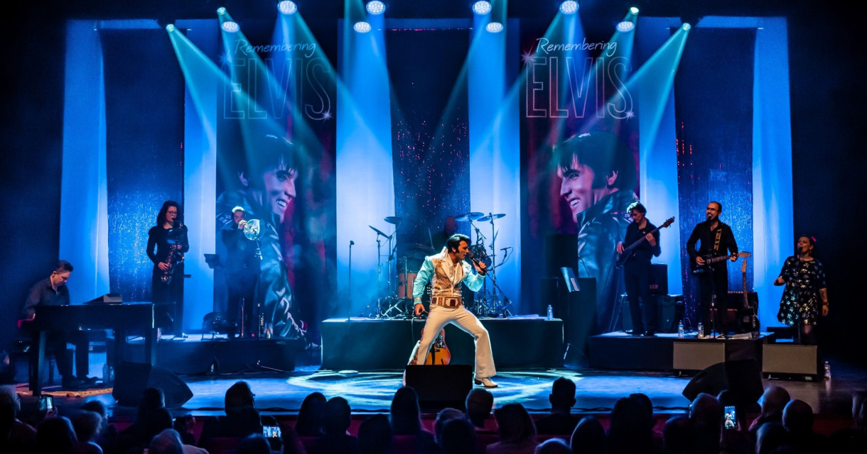 Ein Elvis-Imitator singt auf der Bühne mit Bandmitgliedern.