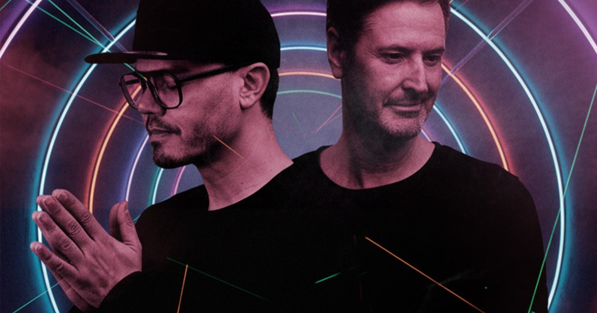 Twee mannen poseren voor een kleurrijke neon achtergrond.