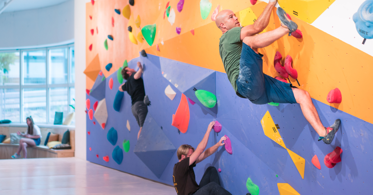 Drie klimmers boulderen op kleurrijke muren in een klimhal.