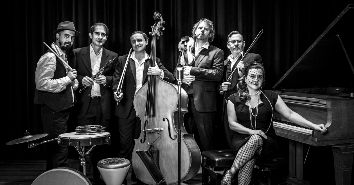 Zeven muzikanten poseren met instrumenten in zwart-wit.