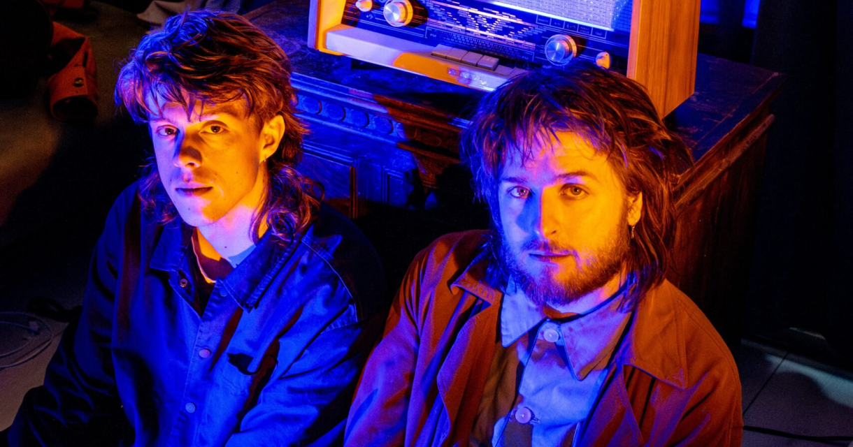 De Dj's zitten op de grond in een ruimte met kleurrijk licht en een vintage radio.