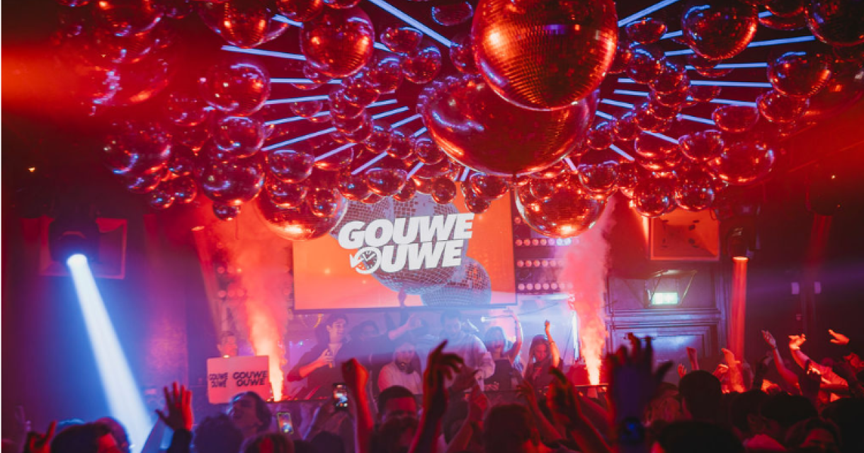 Een levendig nachtclubfeest met dansende mensen onder een glinsterend plafond van discoballen. (c) Gouwe Ouwe