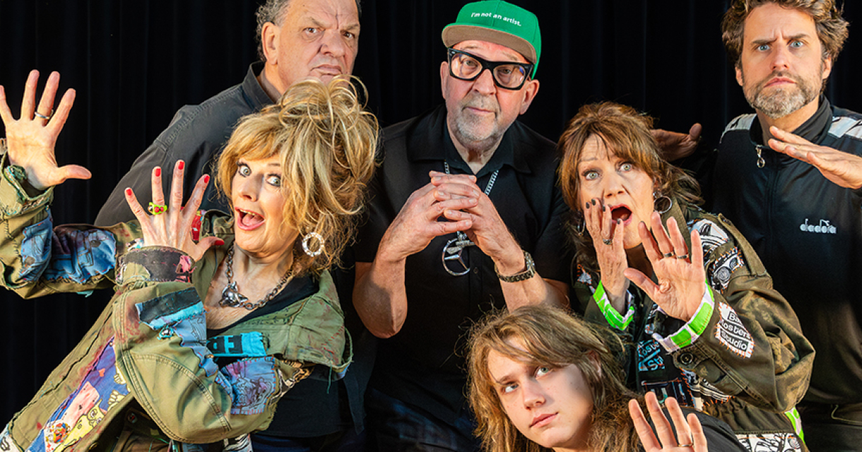 Zes personen poseren met opvallende gezichten en outfits.