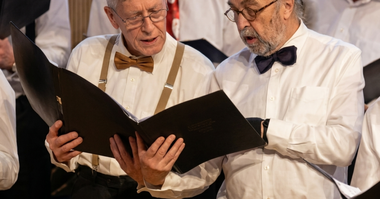 Twee mannen in witte overhemden en vlinderstrik lezen een koorboek.
