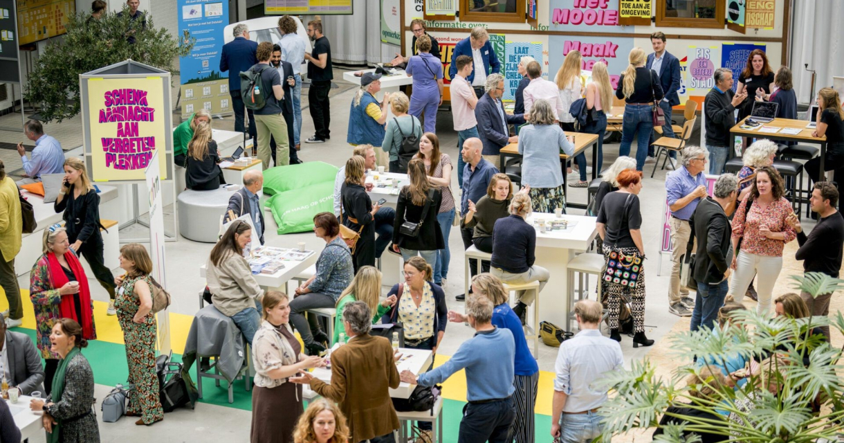 Drukke netwerksessie met mensen in gesprek aan tafels tijdens een evenement in een creatieve, informele setting.