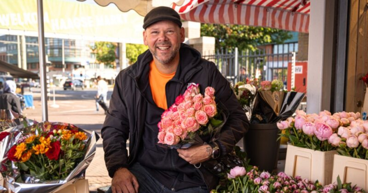 Bloemist stralend omringt met bloemen en een bos roze rozen in de armen. Foto: Joey Kames_credits Fem Schook