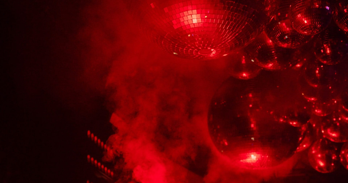 Spiegelbollen hangen boven een verlichte dansvloer in een rode gloed