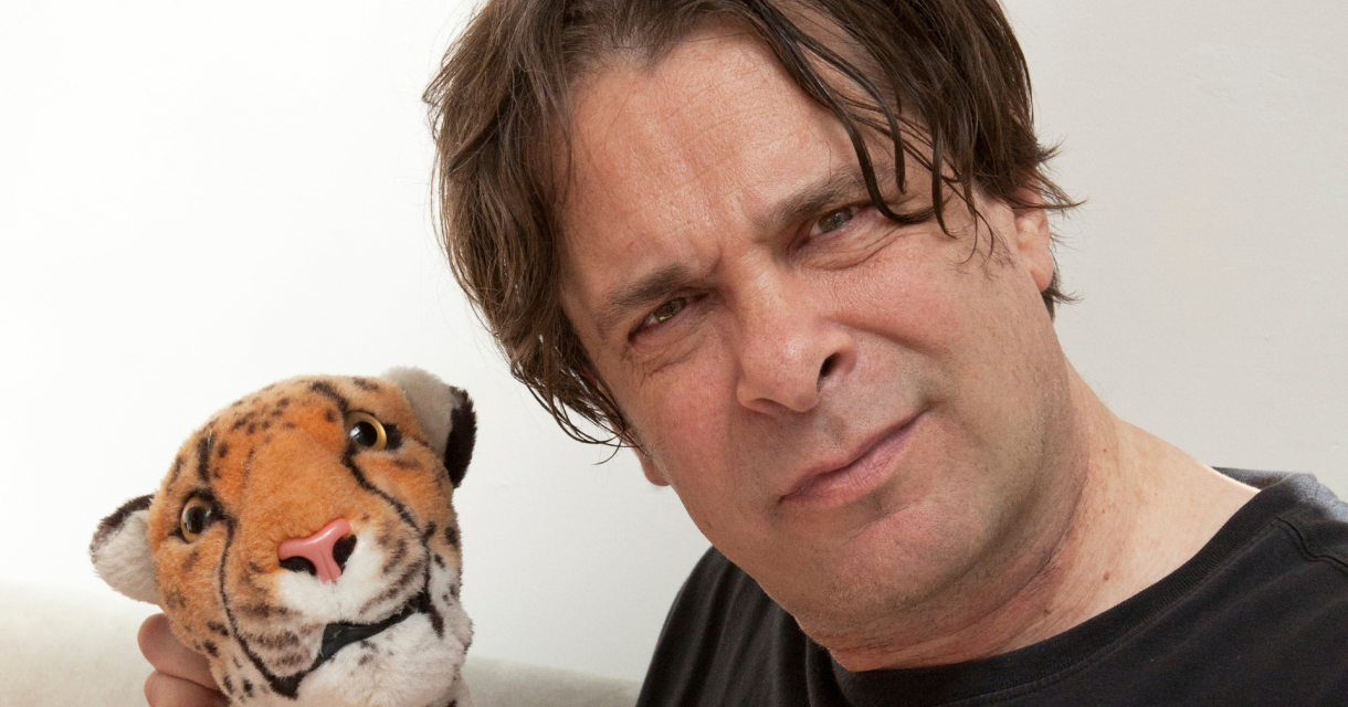 Een man houdt een knuffeltijger vast en kijkt serieus.