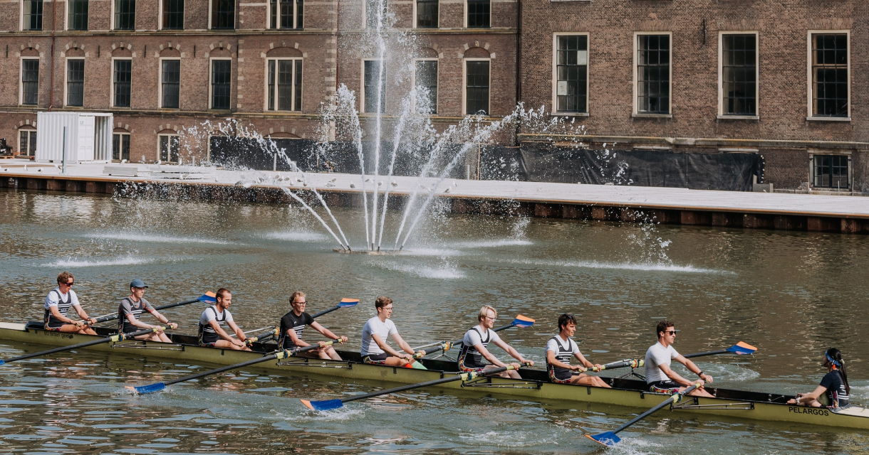 Een roeiteam in het water voor het Binnenhof in Den Haag.