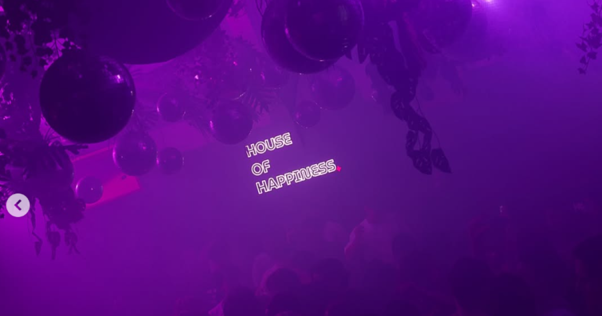 Een drukke feestzaal met paarse verlichting en discoballen. (c) House of Happiness