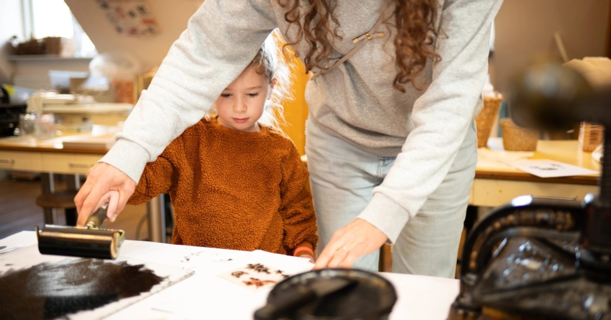 Een kind kijkt toe terwijl een volwassene een roller over papier rolt.