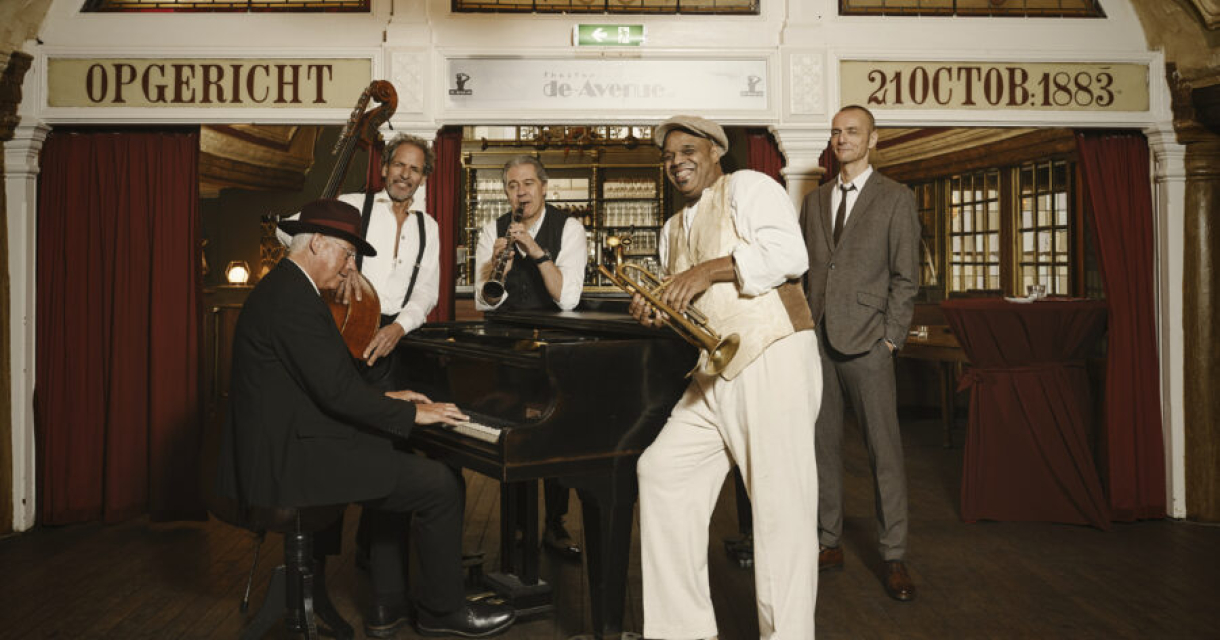 Vijf muzikanten spelen jazz in een café met een piano.