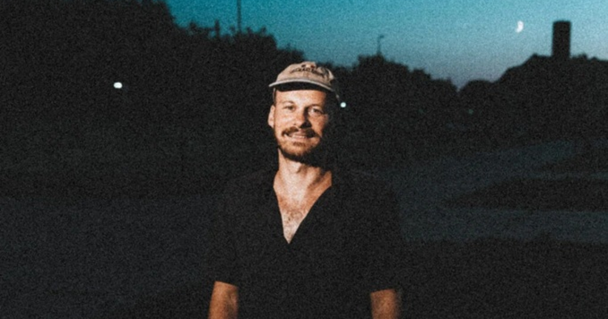 Een man glimlacht in de schemering met een pet op.