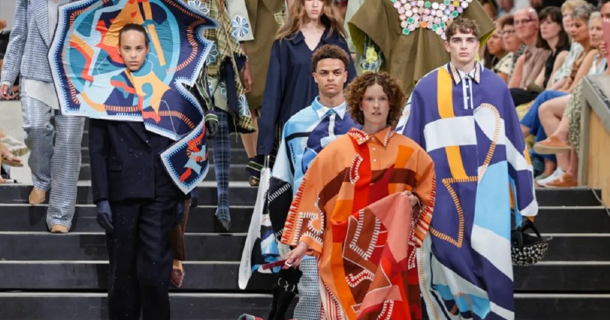 Fashion show featuring diverse outfits. Models walking a runway in striking clothing with prints and colors.