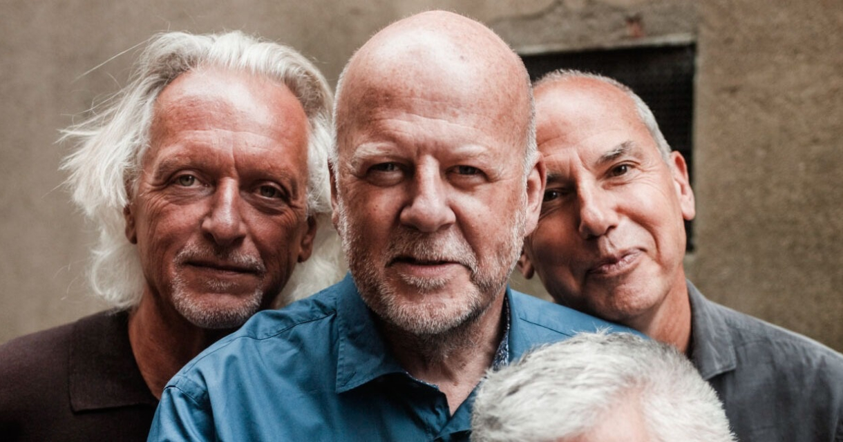Vier mannen poseren samen met glimlachen.
