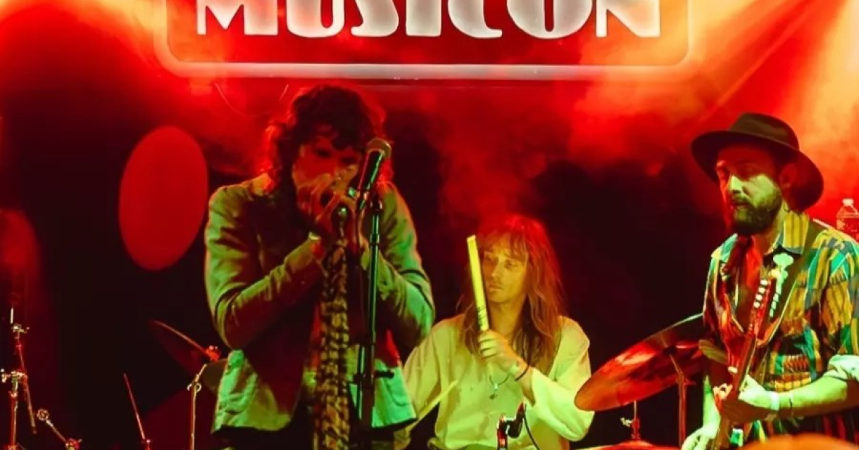 Een band speelt op het podium bij MusicOn, met gekleurde lichten.