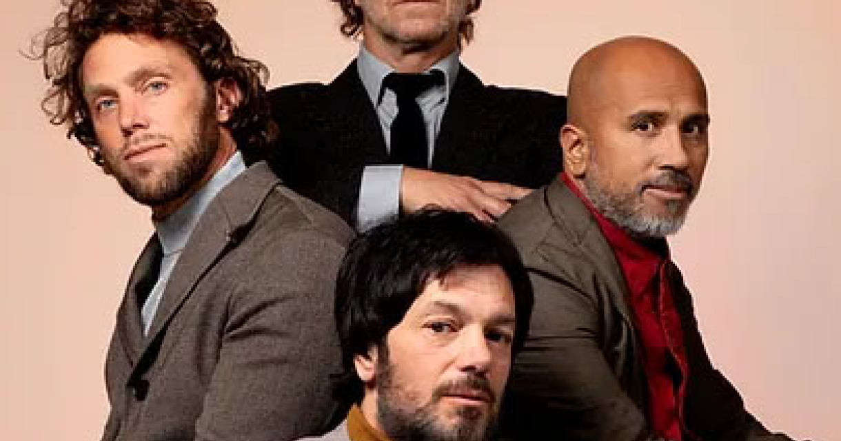 Vier mannen poseren samen, gekleed in trendy outfits.