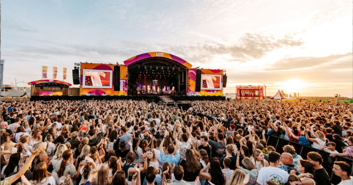 Groot publiek geniet van een muziekfestival bij zonsondergang.