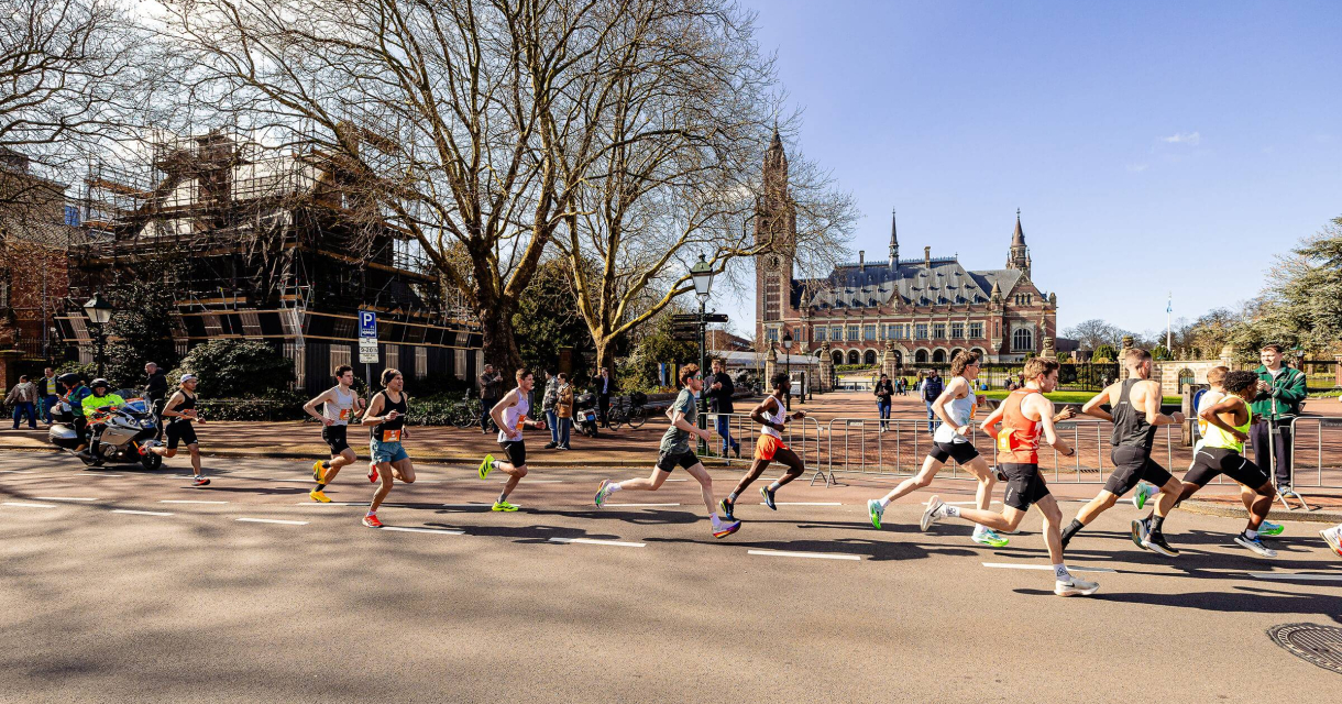 Atleten rennen tijdens een wedstrijd in Den Haag, met het Vredespaleis op de achtergrond.